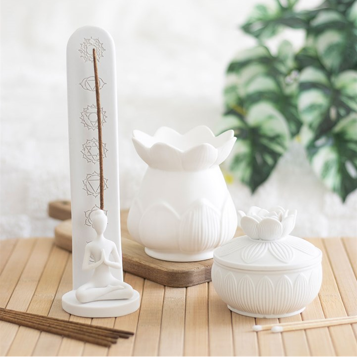 White ceramic incense holder with incense sticks on a wooden surface with a blurred green plant in the background.
