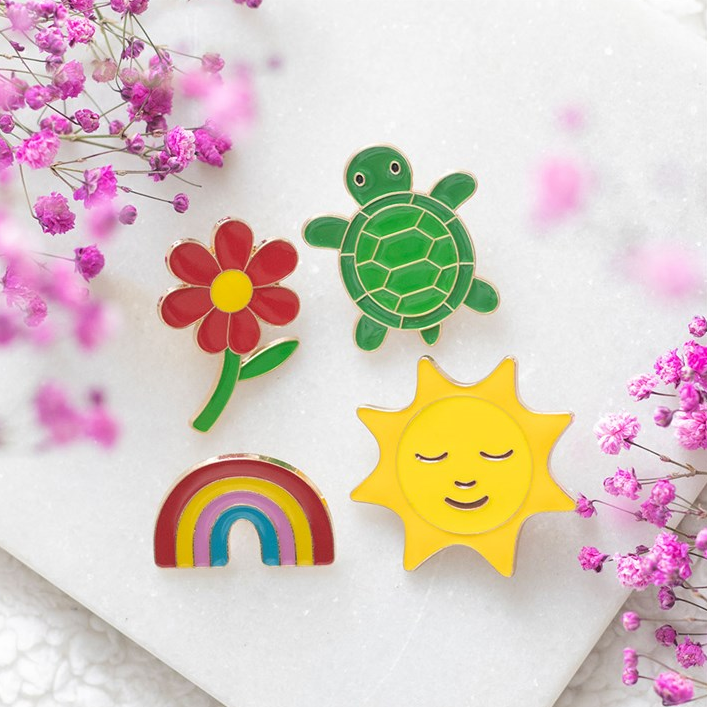 Colorful wooden pins including a turtle, flower, rainbow, and sun on a white surface with pink flowers.
