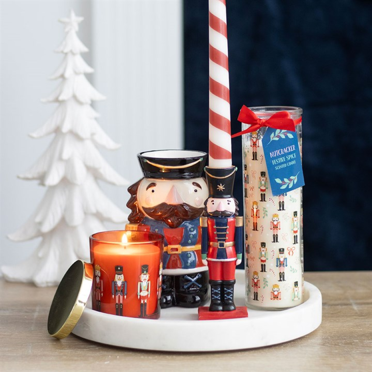 Decorative nutcracker candle holder with a lit candle and a jar of spice mix on a wooden surface.