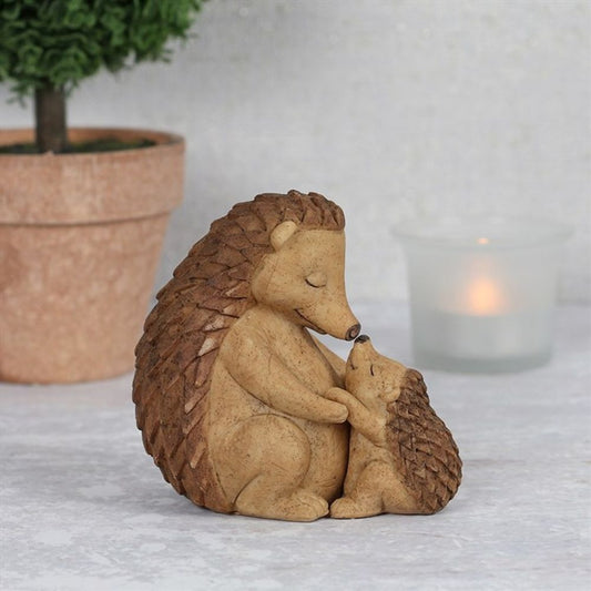 A ceramic ornament featuring a mother hedgehog cuddling her baby, with both figures in a beige color.
