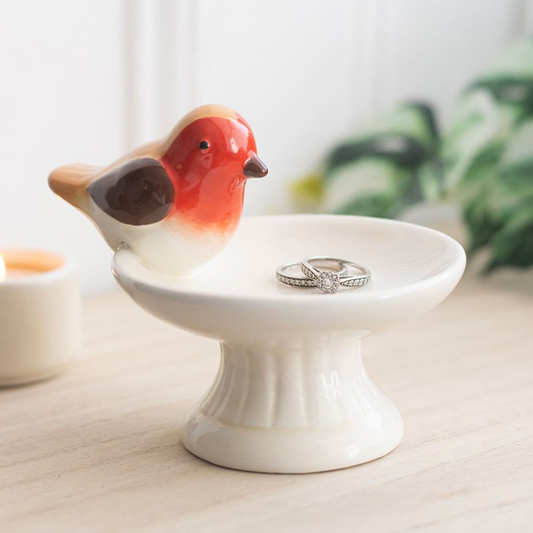 Ceramic robin bird on a white stand with rings, against a blurred indoor background.