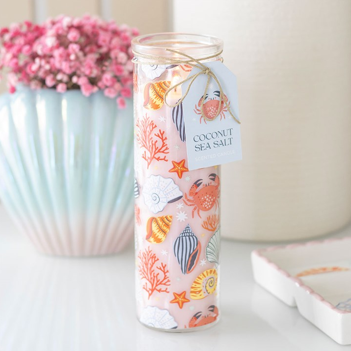 Candle in a decorative glass jar with a label, placed on a surface with a blurred background.
