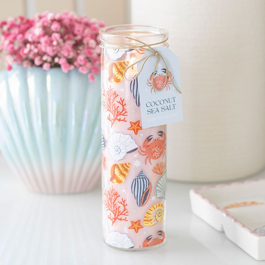 Candle in a decorative glass jar with a label, placed on a surface with a blurred background.
