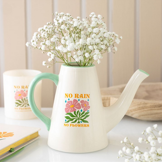 White teapot with floral design and text, filled with white flowers on a light background.