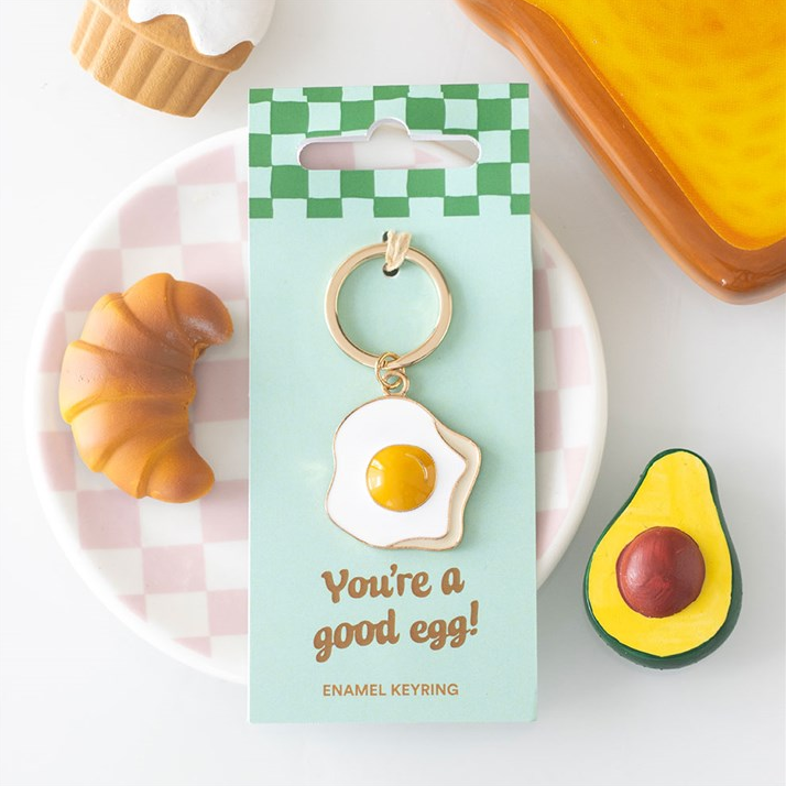 Keychain with 'You're a good egg!' message on a checkered card, surrounded by food-themed items.