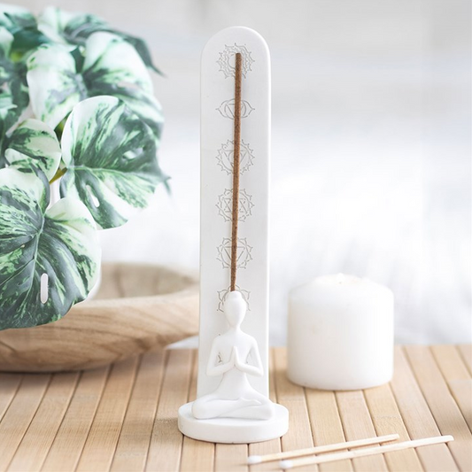 White incense holder with figure holding a yoga pose, plant in the background