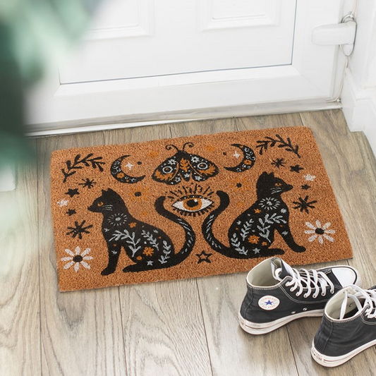 Decorative doormat with cat and moon design on a wooden floor, with shoes at the entrance.