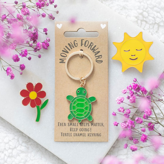Keychain with turtle design on a decorative card with flowers and sun, on a white background.