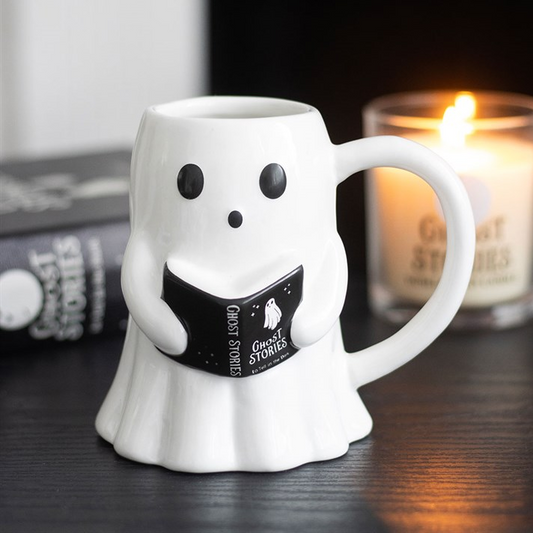 Ghost-shaped mug holding a book with a candle in the background