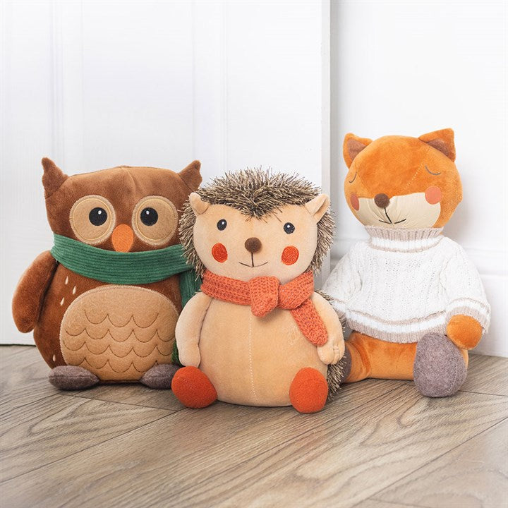 Three plush doorstops shaped like an owl, hedgehog, and fox sitting on a wooden floor.