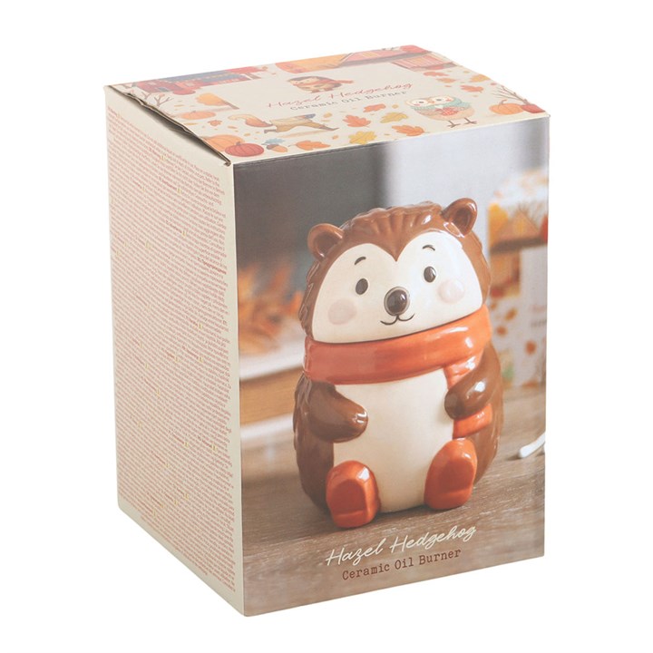 Ceramic oil burner shaped like a hedgehog in a packaging box with a scenic background.