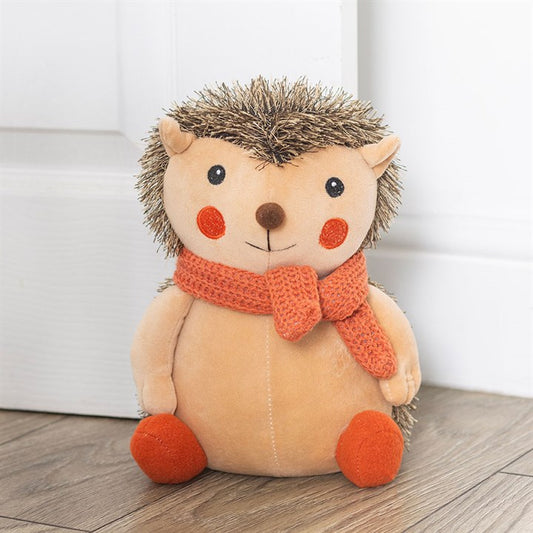 Plush hedgehog doorstop with an orange scarf on a wooden floor.