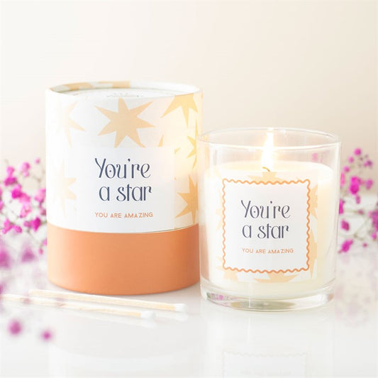 A candle and it's packaging box with 'You're a star' and 'You are amazing' text on a light background.