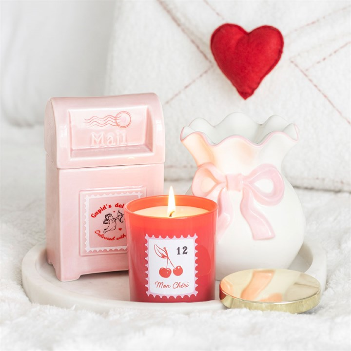 Candle with a heart-shaped wick holder and pink mailbox on a white surface