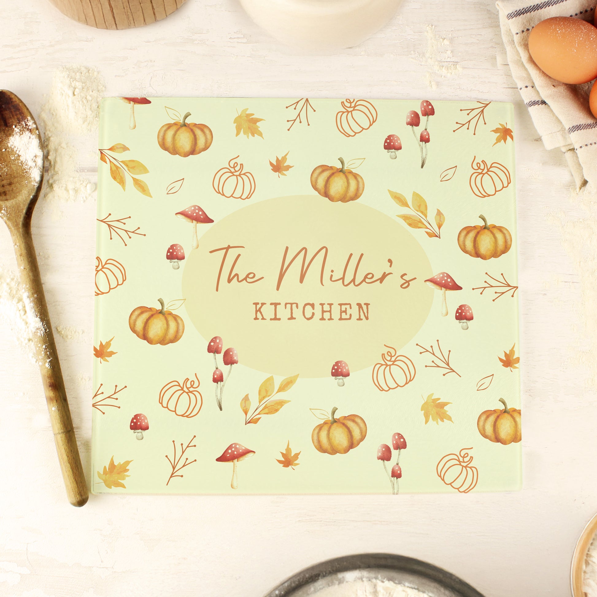 Square glass chopping board with autumn design and 'The Miller's Kitchen' text on it.