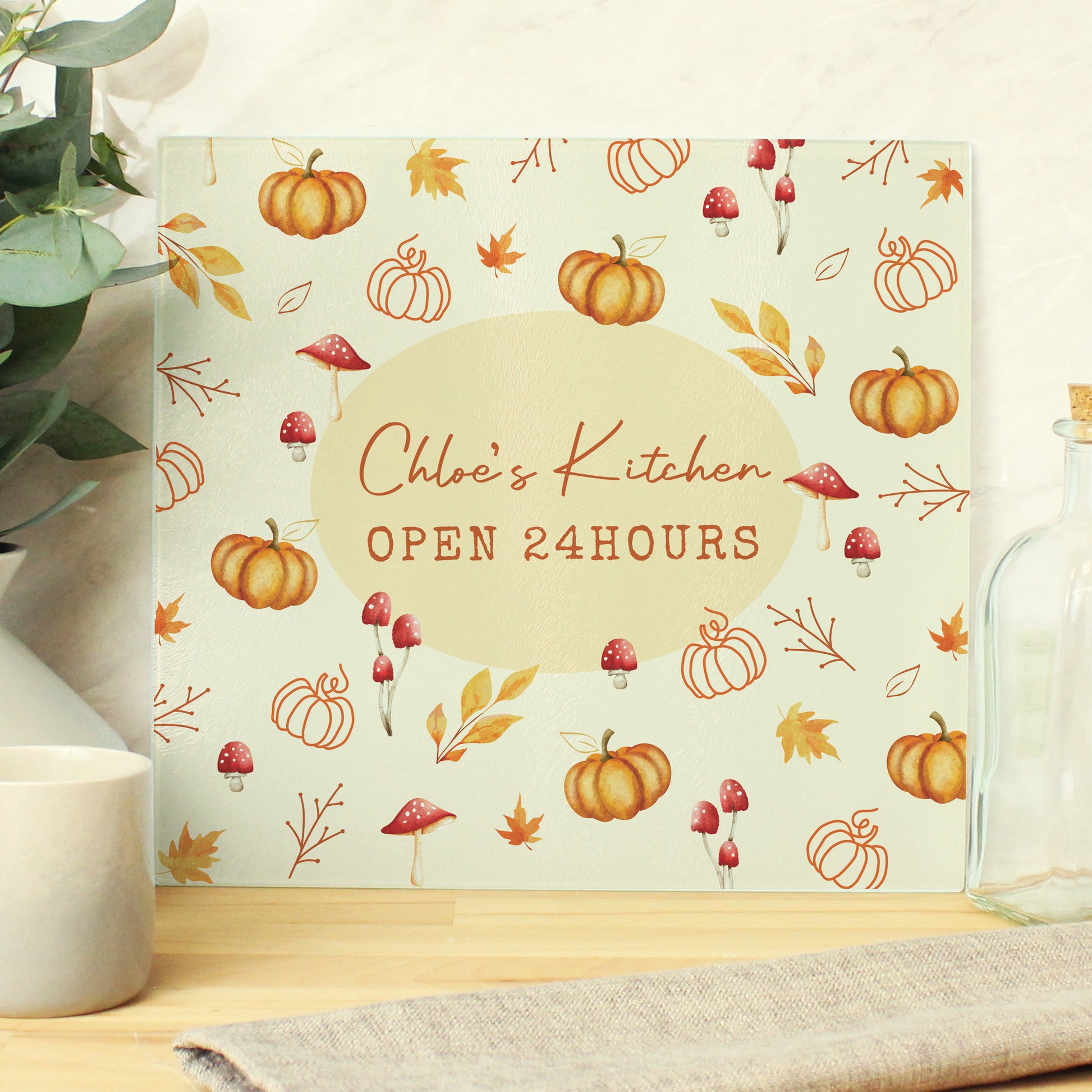 Glass cutting board with autumn pumpkin and mushroom design and 'Chloe's Kitchen Open 24 Hours' text on a wooden surface. Wording can be personalised.