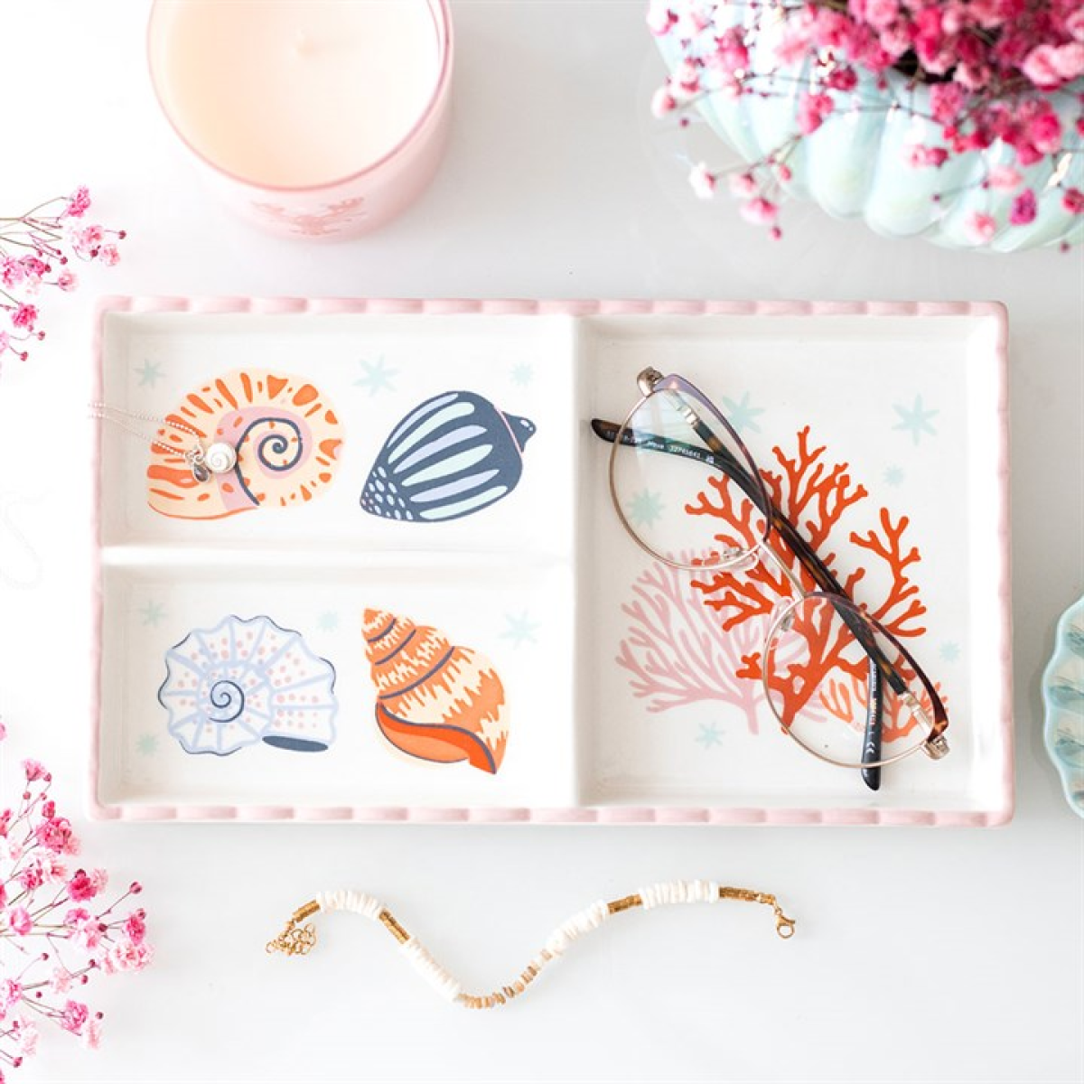 Decorative jewelry tray with shell and coral designs on a white surface with flowers.