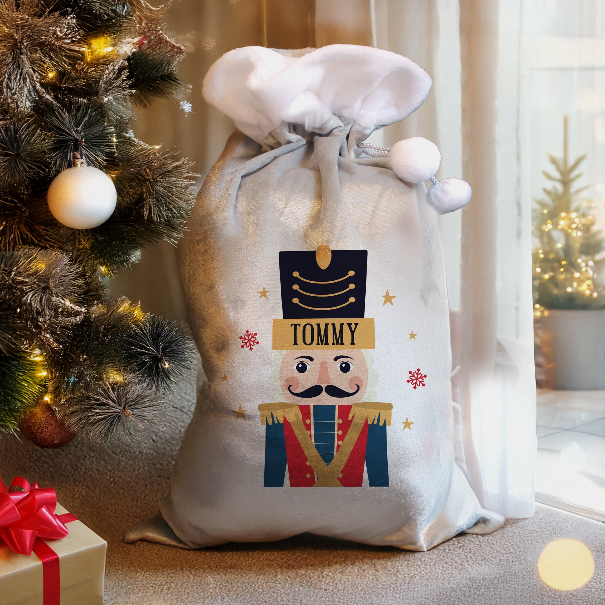 Decorative Christmas sack with a nutcracker design and 'Tommy' text, placed next to a Christmas tree and gift.