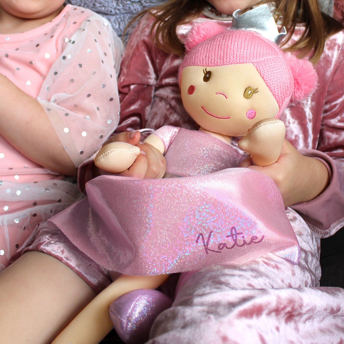 Child holding a plush toy with 'Katie' on it, wearing pink outfit.
