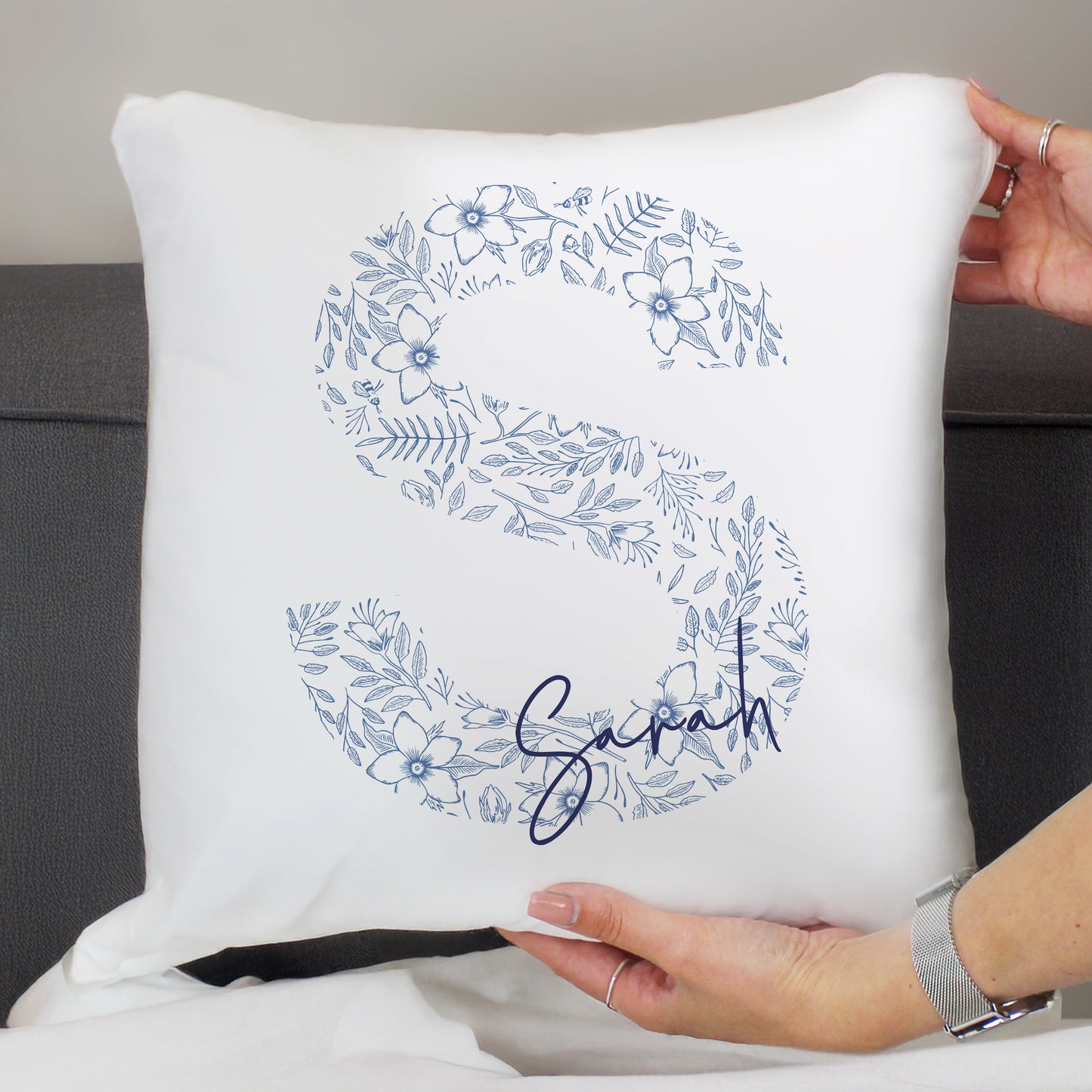 White pillow with blue floral design and name 'Sasha' held by a person.