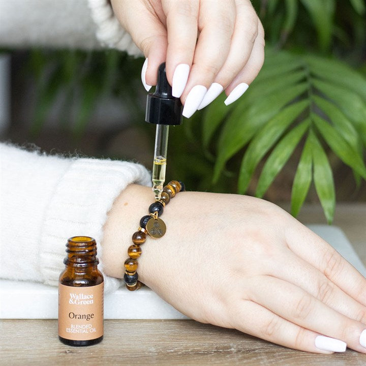 Person applying orange essential oil to a wrist with a dropper and bottle on a wooden surface.
