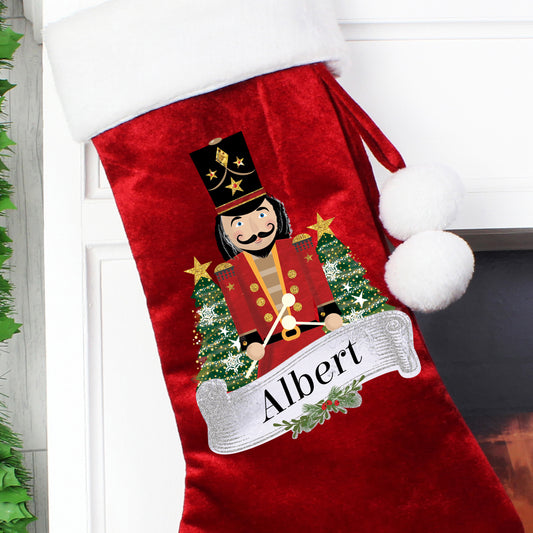 Red Christmas stocking with a Nutcracker design and 'Albert' text, hanging on a fireplace.