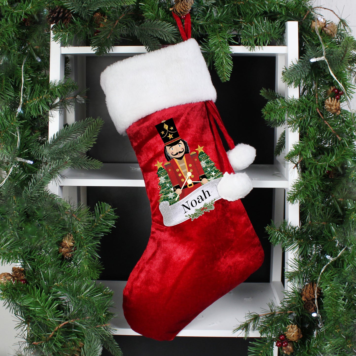 Red Christmas stocking with a Nutcracker design and 'Noah' text, hanging on a tree.