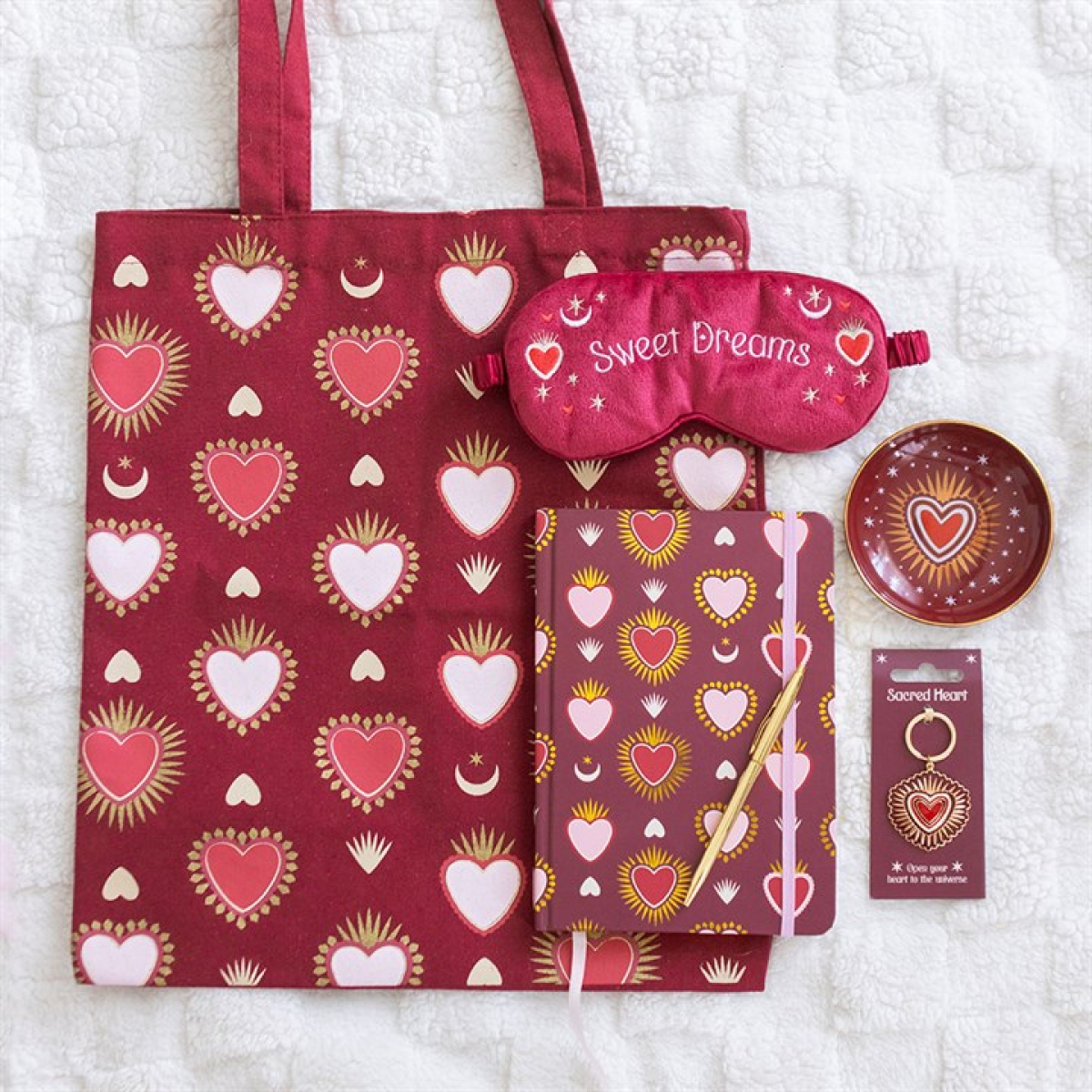 Set of red heart-patterned products including a tote bag, sleep mask, notebook, and trinket dish on a white background.