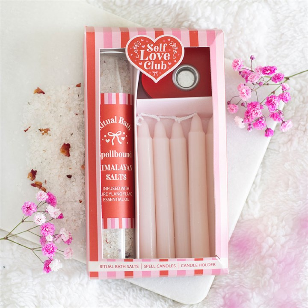 Packaged product from Self Love Club with candles and bath salts on a textured surface with flowers.