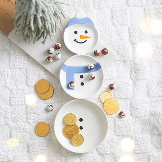Snowman-themed decorative set with small bowls and coins on a textured white surface.