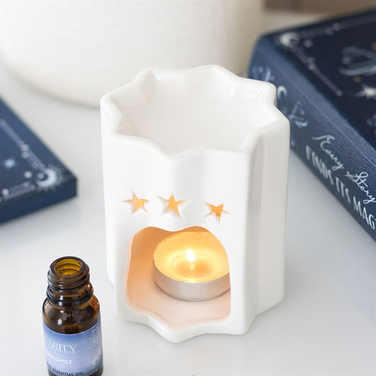 White ceramic oil burner with a lit candle and a bottle of Clarity coconut oil on a white surface.