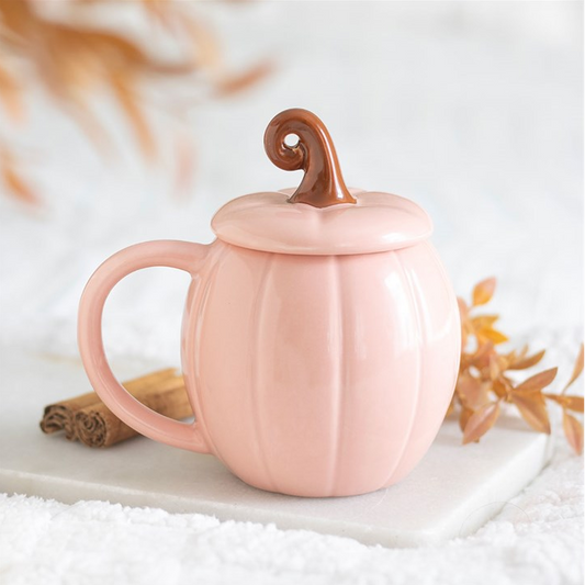 Pink pumpkin-shaped mug with a lid on a white surface with autumn leaves.