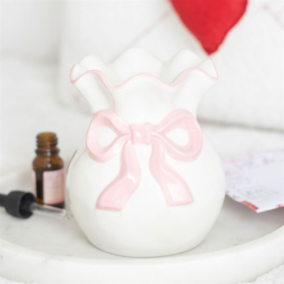 White ceramic oil and wax burner with a pink bow on a white surface with a blurred background