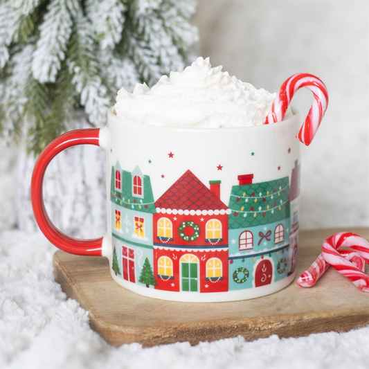 Mug with Christmas village design filled with hot chocolate and whipped cream, surrounded by candy canes and a snowy background.